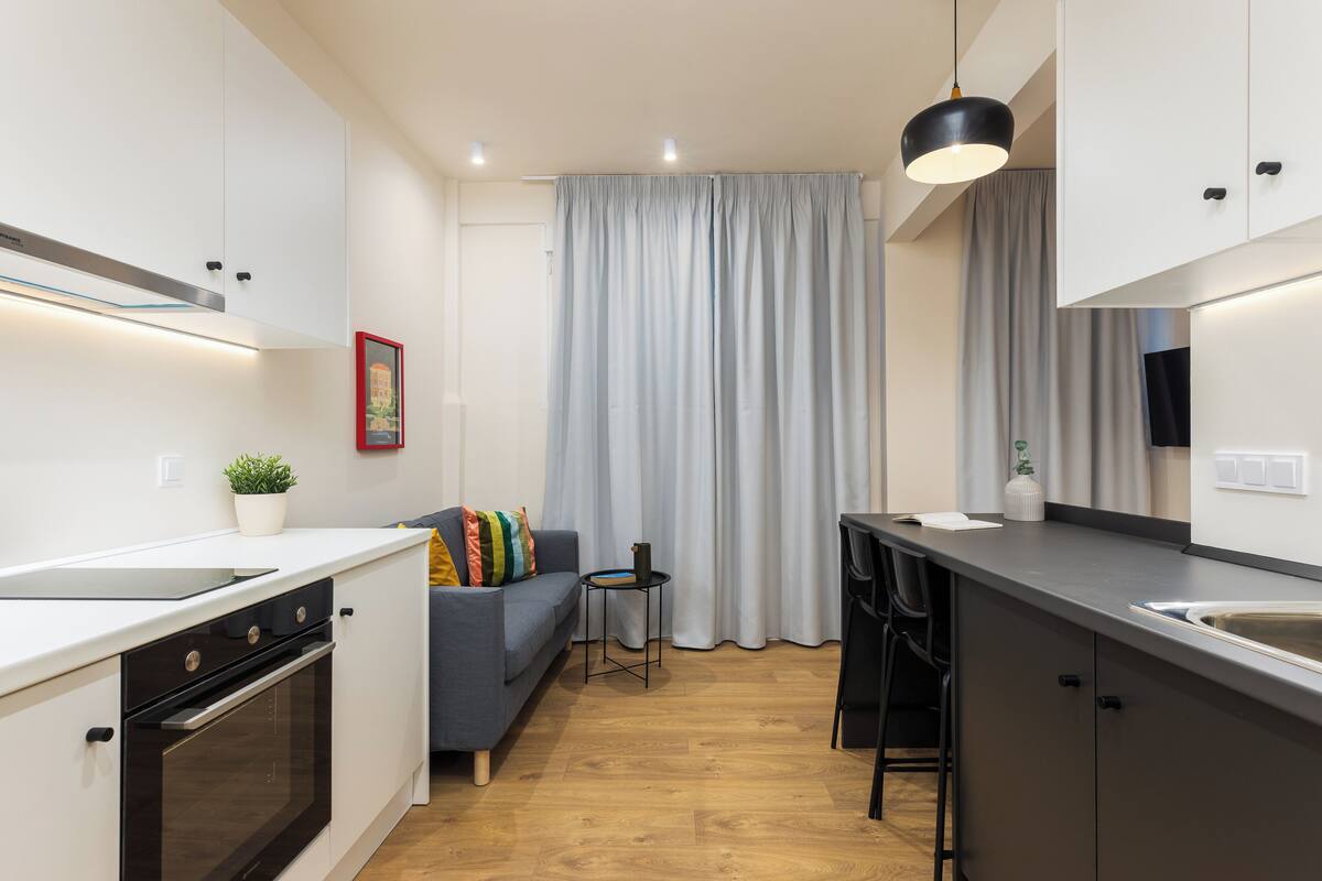 Una cucina compatta con elettrodomestici moderni, una zona pranzo con divano e vista attraverso un'ampia finestra con tende.