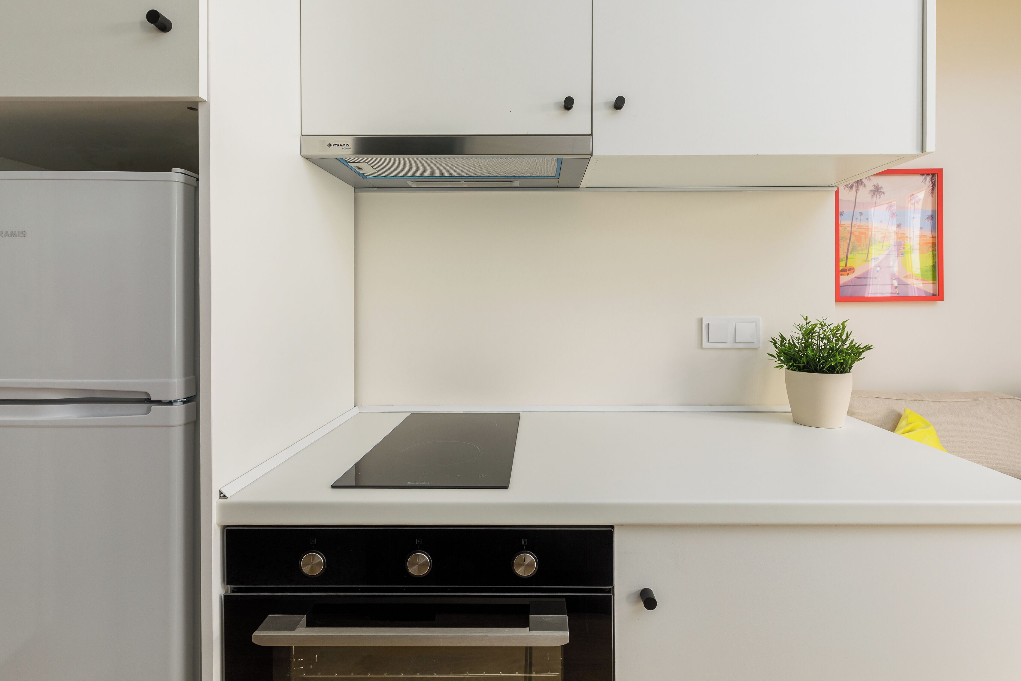 A modern kitchen with a built-in oven, a stainless steel refrigerator, and a wall-mounted plant.