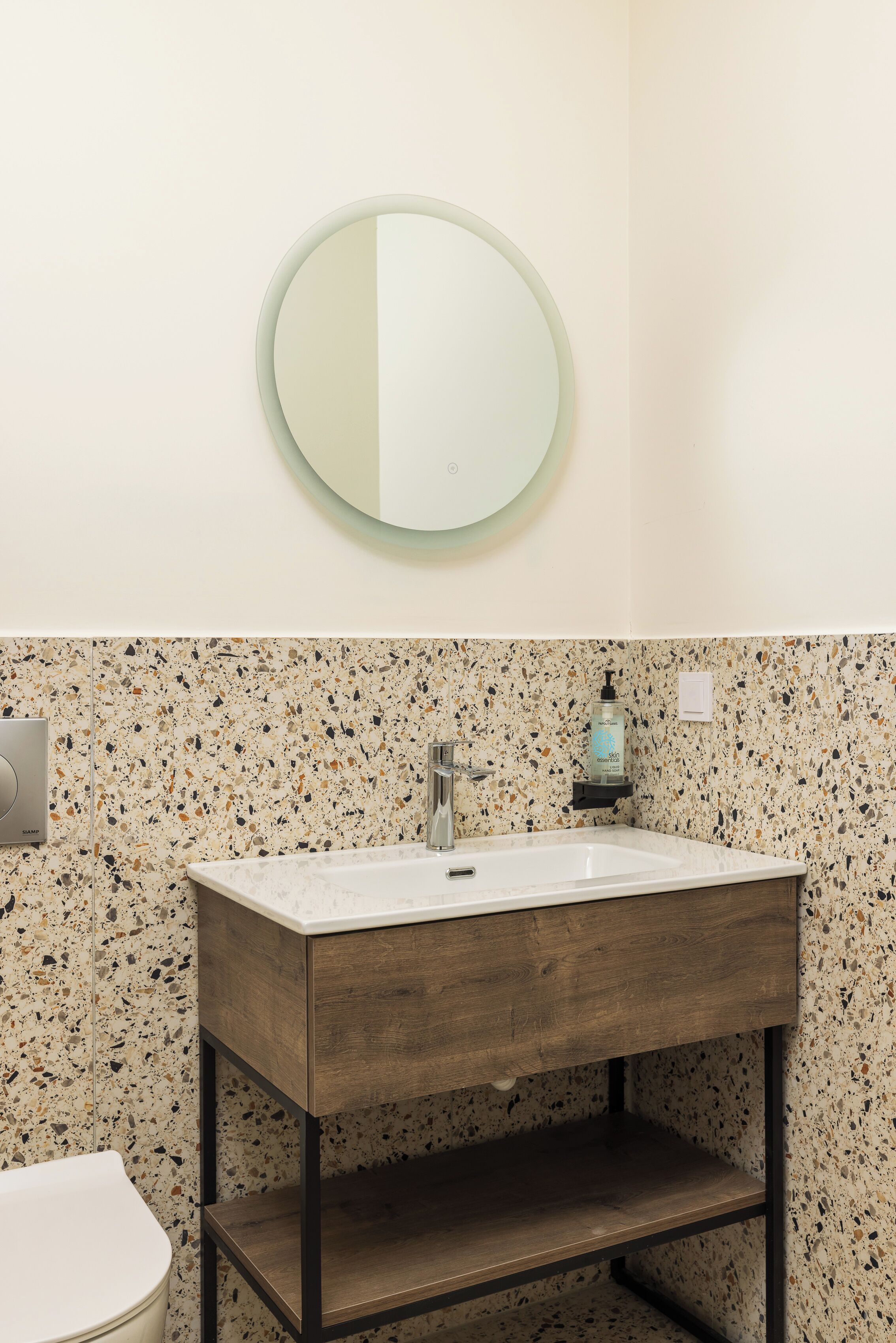 Une salle de bain avec un lavabo blanc, un meuble-lavabo en bois et un pare-éclaboussures à motifs.