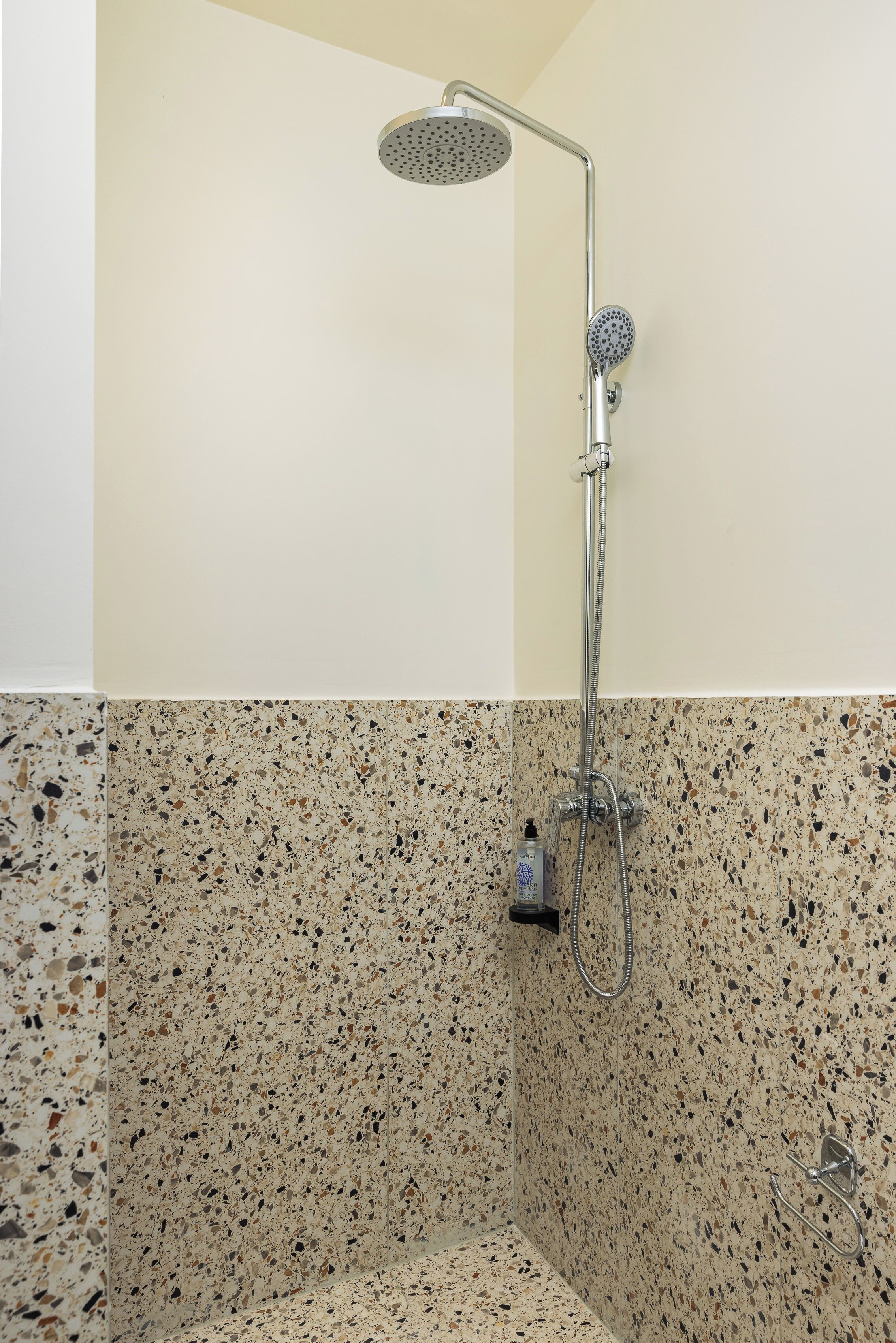 A shower with a handheld showerhead and a wall-mounted faucet, set against a speckled tile wall.