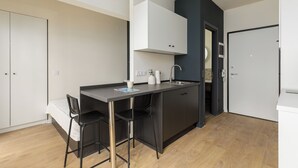 Een kleine keuken met een centraal eiland, twee barkrukken, een wit kastje en een zwarte plafondlamp.