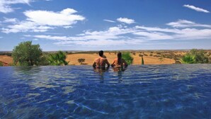 A swimming pool with clear blue water, surrounded by greenery and a desert landscape in the background. - Rosemary Room (Póvoa de São Miguel)
