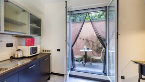 Une cuisine compacte équipée d’un four à micro-ondes, d’une bouilloire et d’une petite table avec des chaises. Une porte-fenêtre coulissante donne accès à un espace extérieur aménagé avec une table et des chaises.