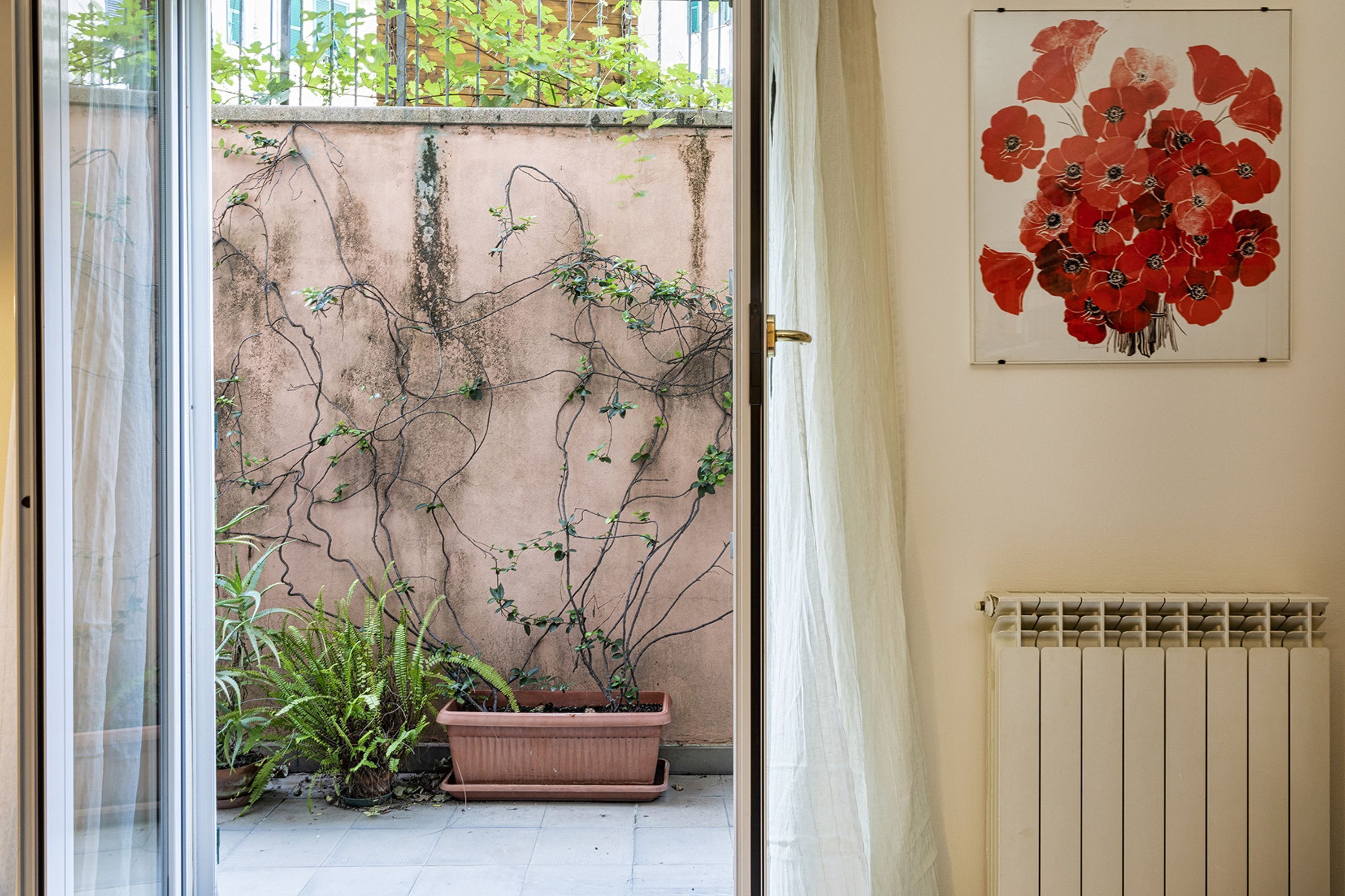 Une pièce dotée d’une porte-fenêtre coulissante donnant sur un balcon agrémenté de plantes en pot et d’un radiateur fixé au mur.