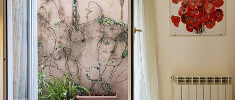 Une pièce dotée d’une porte-fenêtre coulissante donnant sur un balcon agrémenté de plantes en pot et d’un radiateur fixé au mur.