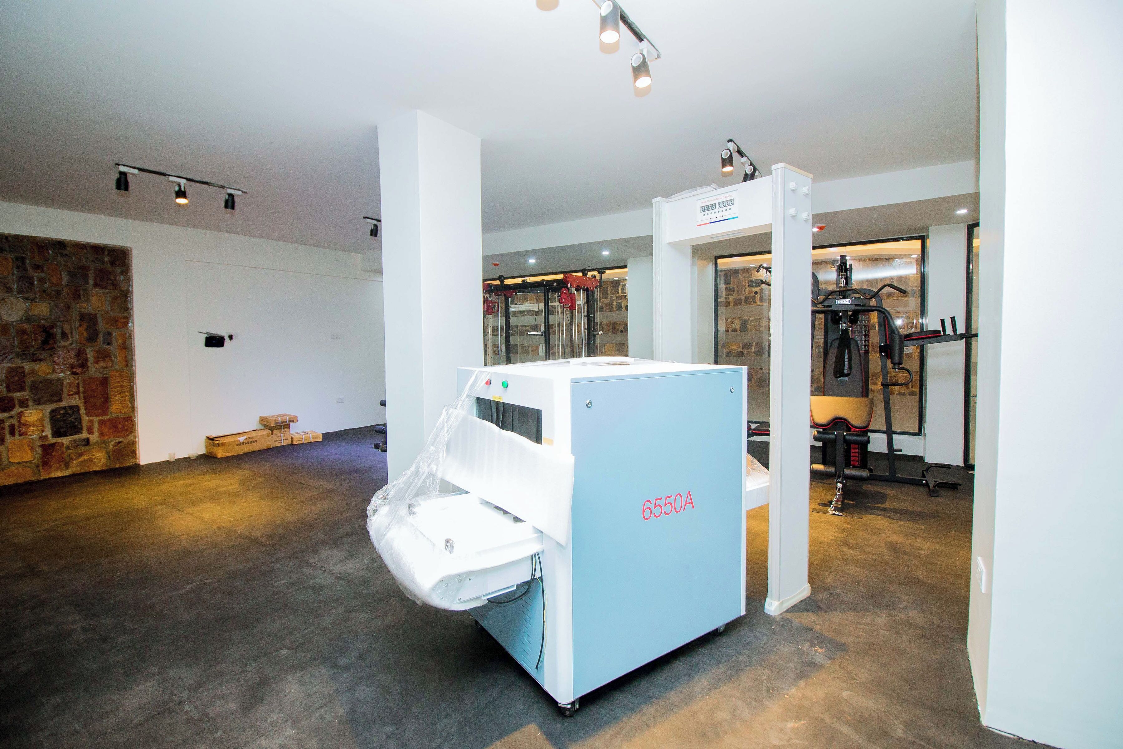 A room with a large industrial machine labeled 6550A, a stone wall, and a door leading to another area with exercise equipment.