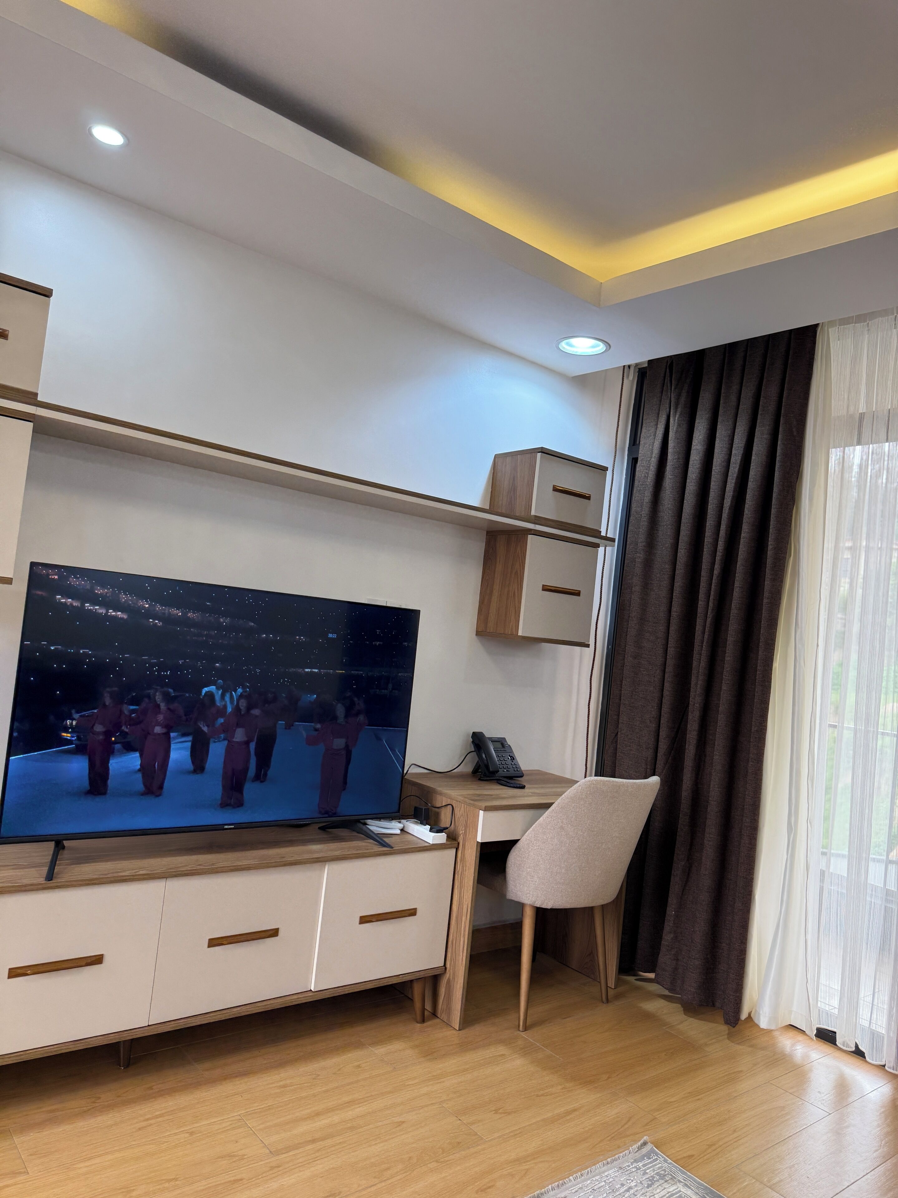 A modern living room with a flat-screen TV, wooden furniture, a desk, and a chair.