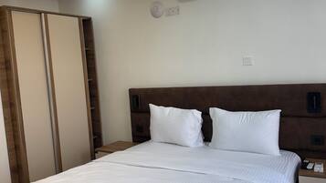 A modern hotel room with a large bed, wooden headboard, bedside tables, an air conditioning unit, and a ceiling light fixture.