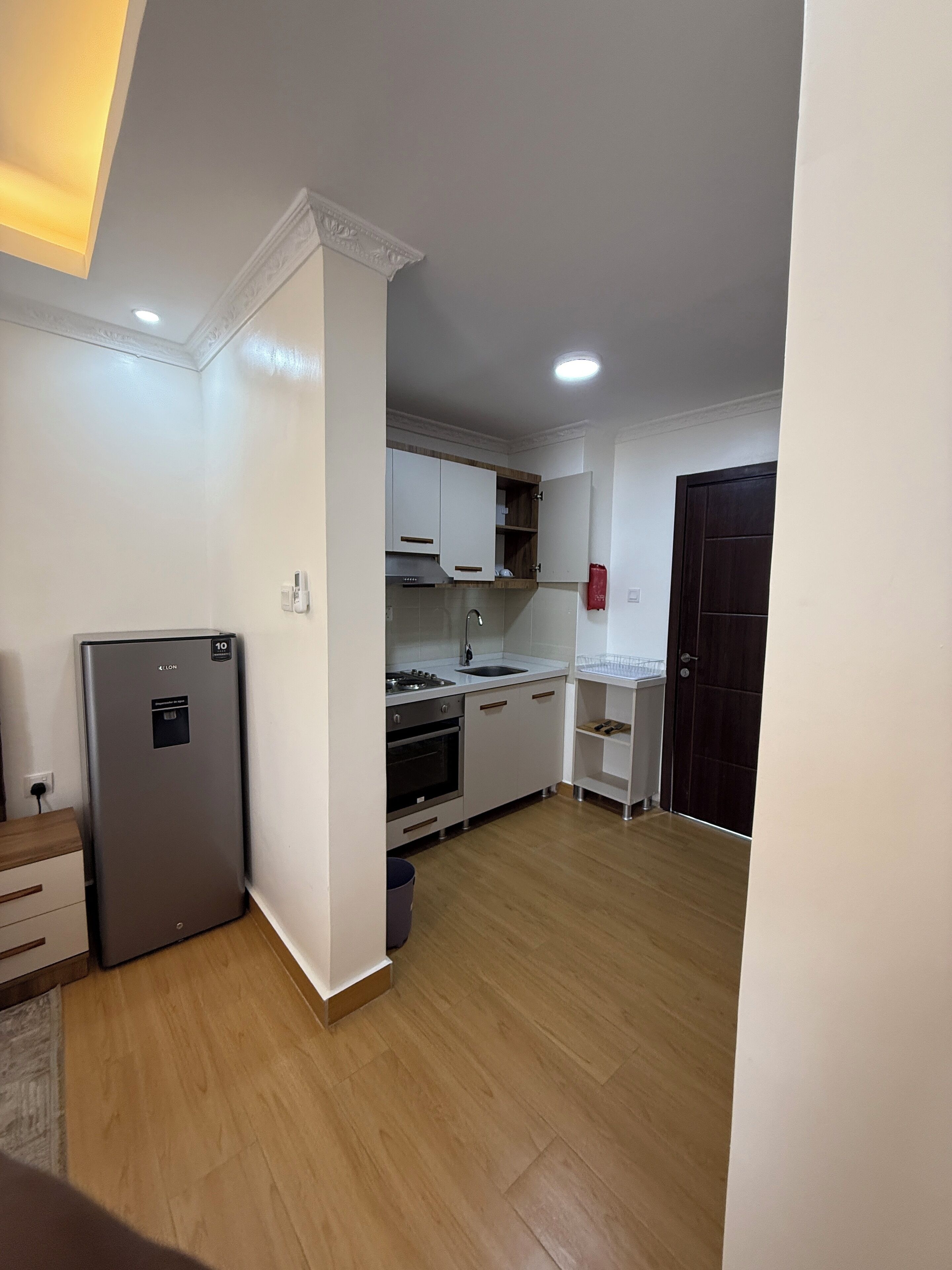 A compact kitchen with white cabinets, a stainless steel refrigerator, a built-in oven, and a sink.