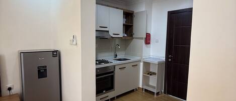A compact kitchen with white cabinets, a stainless steel refrigerator, a built-in oven, and a sink.