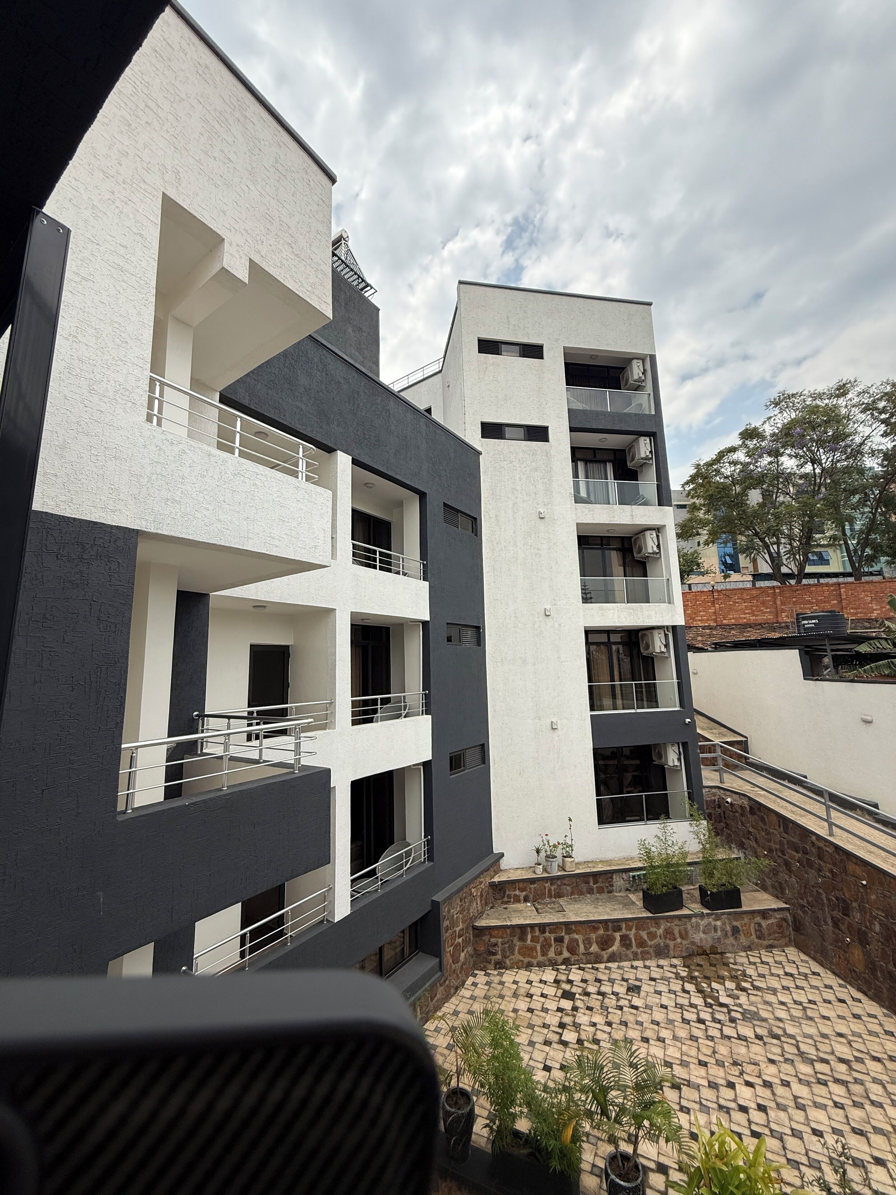A multi-story building with balconies, a courtyard with potted plants, and a stone wall.
