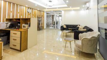 A modern hotel lobby with a wooden reception desk, a black sofa, and a glass partition.