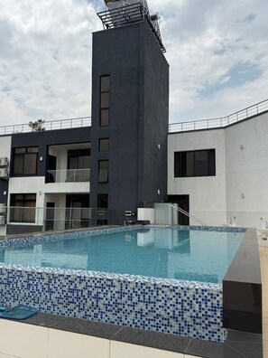 A modern hotel with a swimming pool, a tall black building, and a white building with balconies. - Cascadia Serviced Apartments (Kigali)