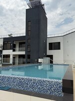 A modern hotel with a swimming pool, a tall black building, and a white building with balconies.