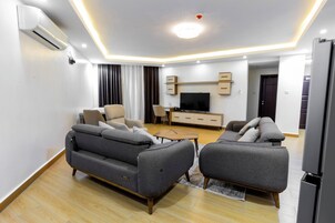 A modern living room with two grey sofas, a flat-screen TV, a wooden coffee table, and a built-in entertainment unit.