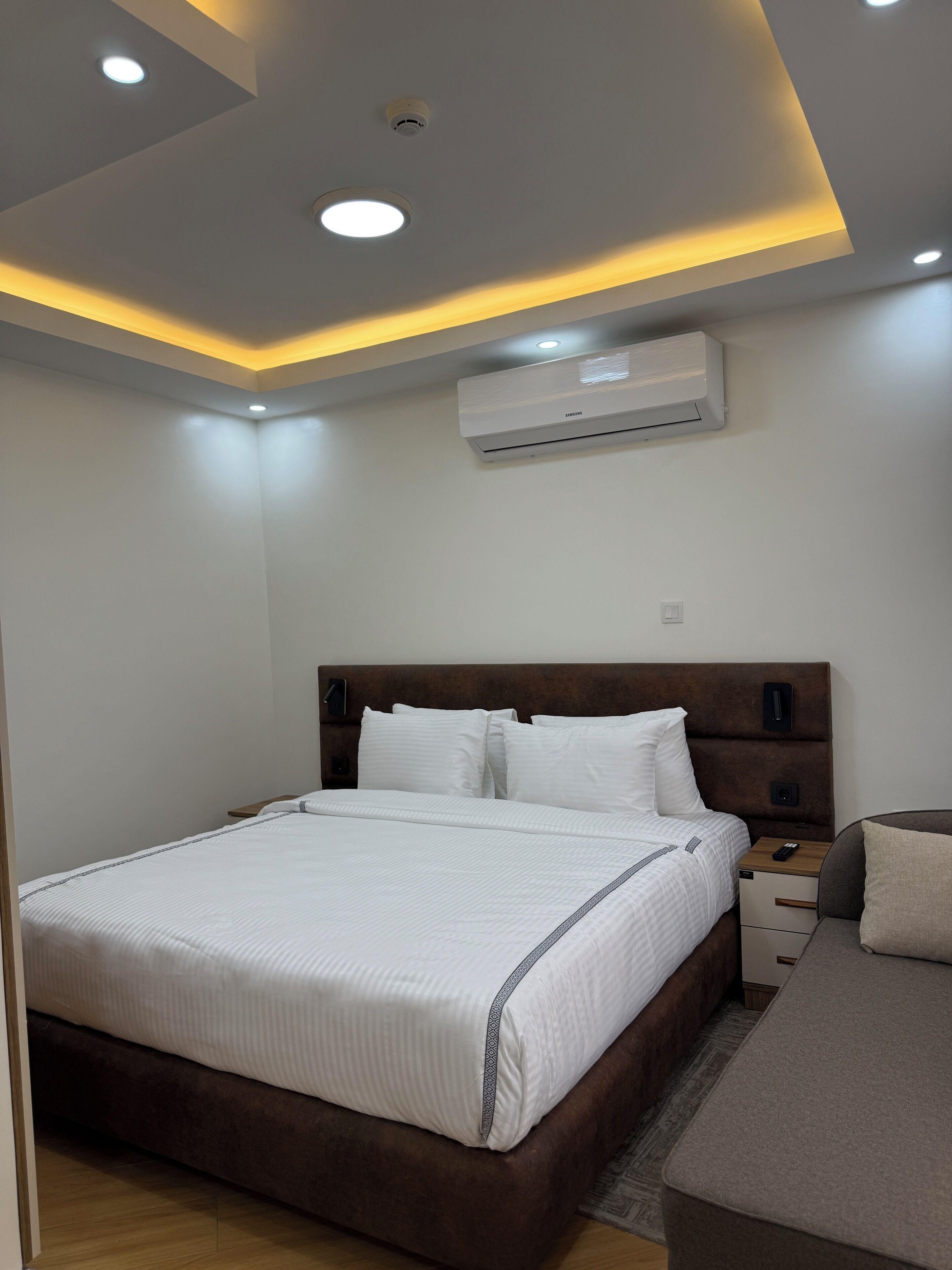 Un dormitorio moderno con una cama grande, una mesita de noche, un sofá y un equipo de aire acondicionado.