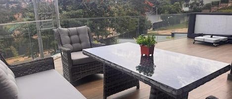 A balcony with wicker furniture, a glass table, and a potted plant.