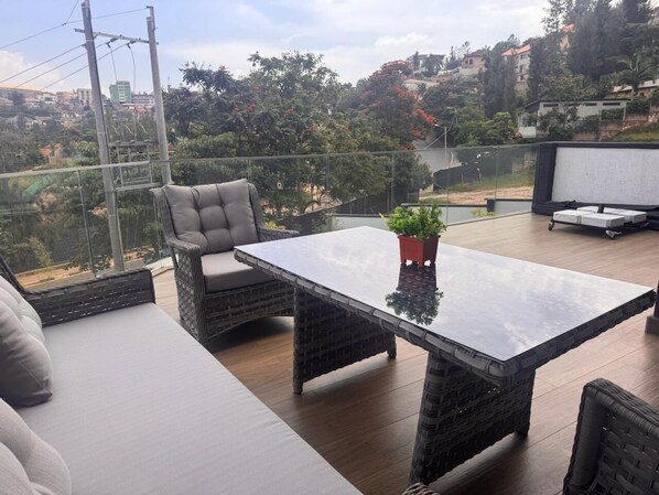 A balcony with wicker furniture, a glass table, and a potted plant. - Cascadia Serviced Apartments (Kigali)