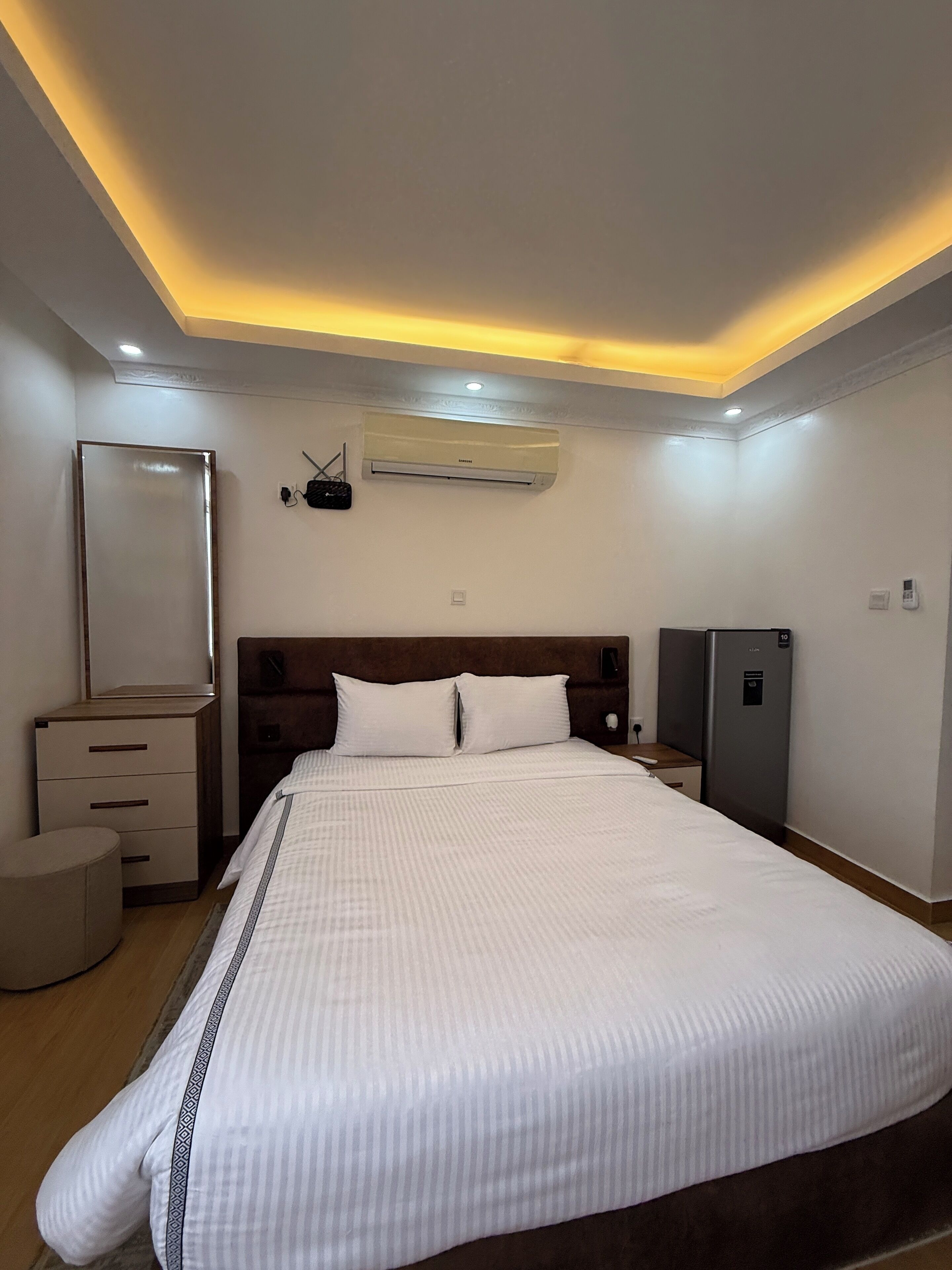 Una habitación de hotel con una cama grande, un aparador, un espejo, un equipo de aire acondicionado y un mueble auxiliar pequeño.