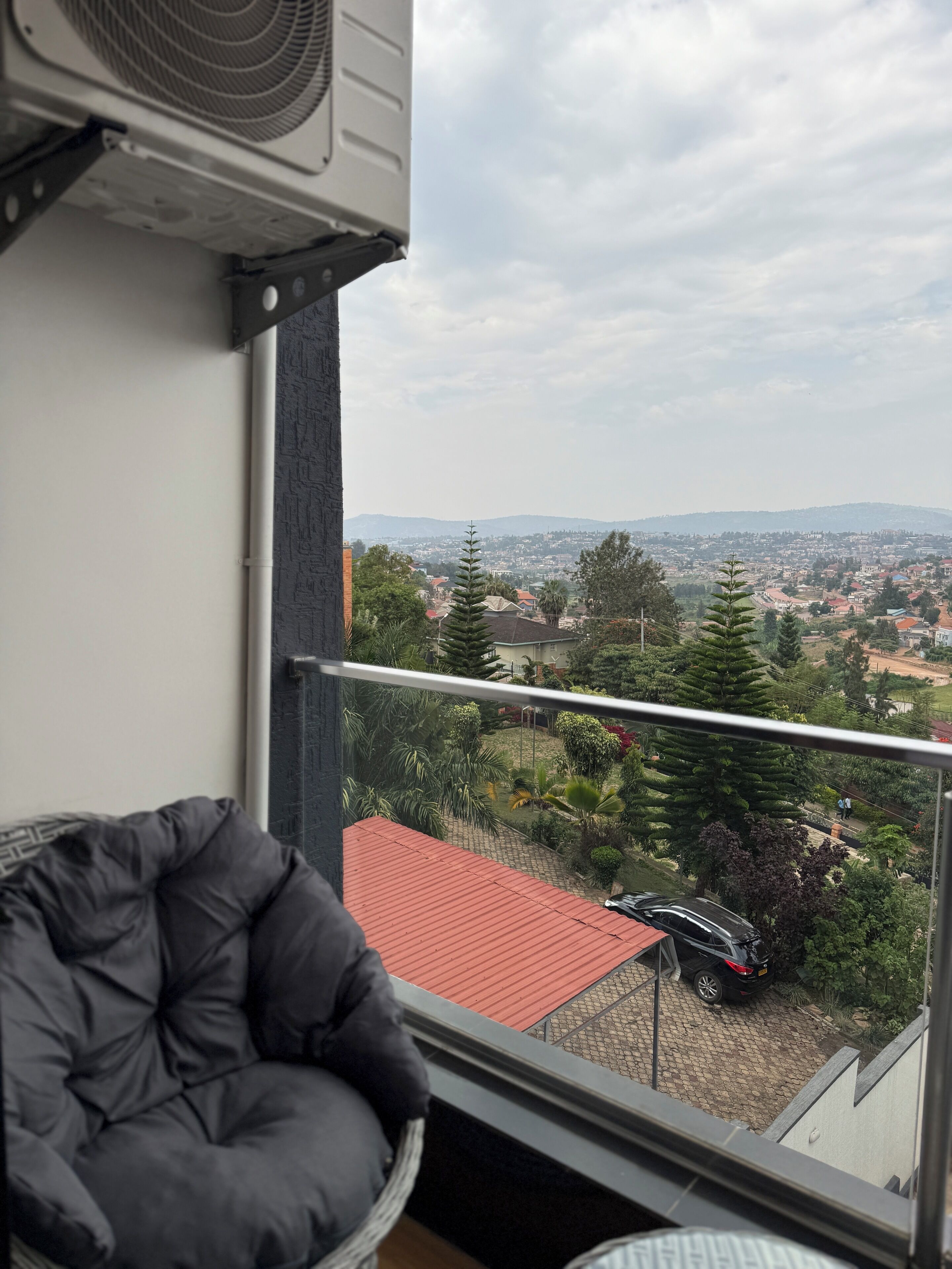 Un balcon donnant sur un quartier résidentiel, un immeuble avec un toit rouge et une voiture garée.