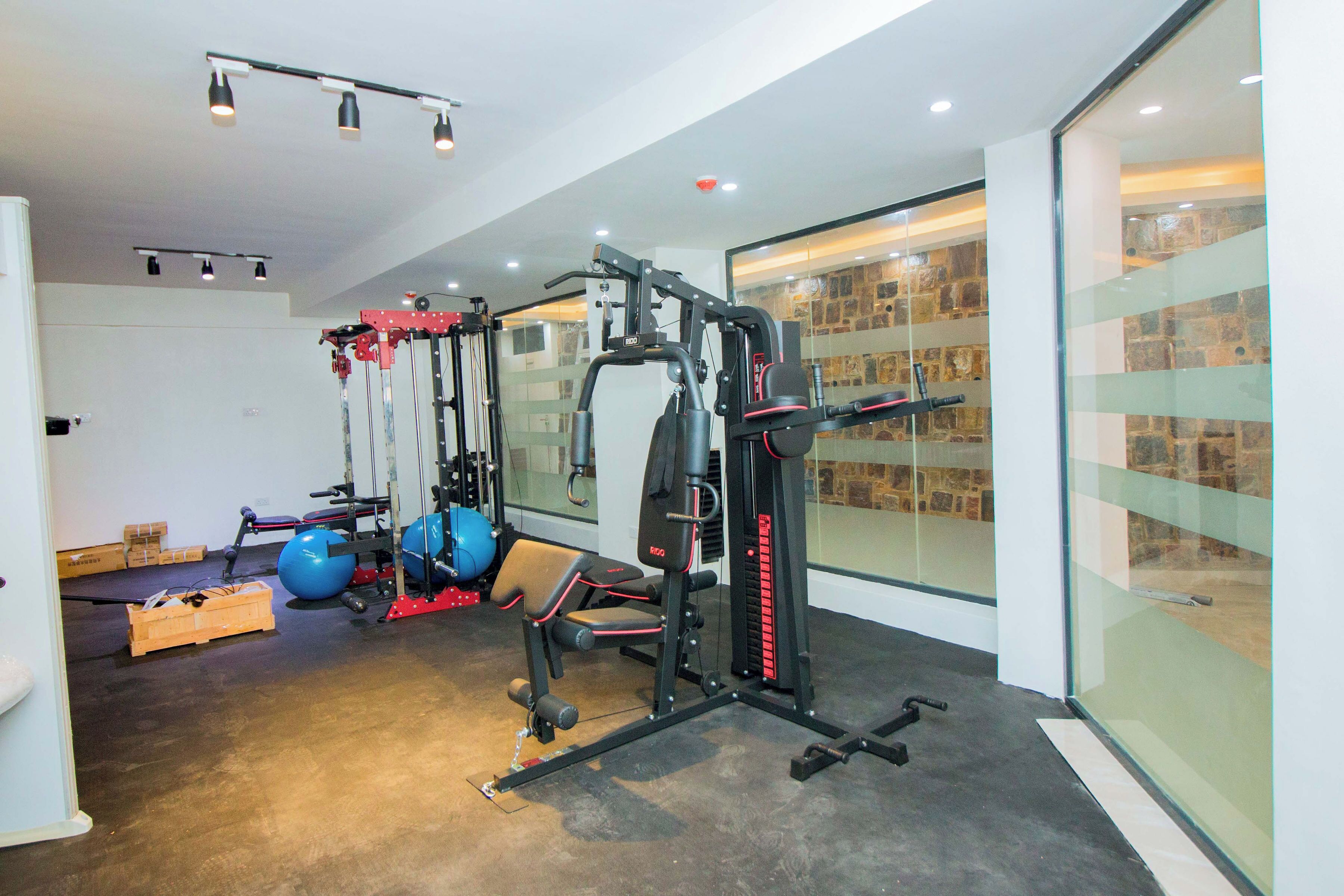 A modern gym with various exercise equipment, a large mirror, and a stone wall.
