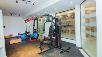 A modern gym with various exercise equipment, a large mirror, and a stone wall.