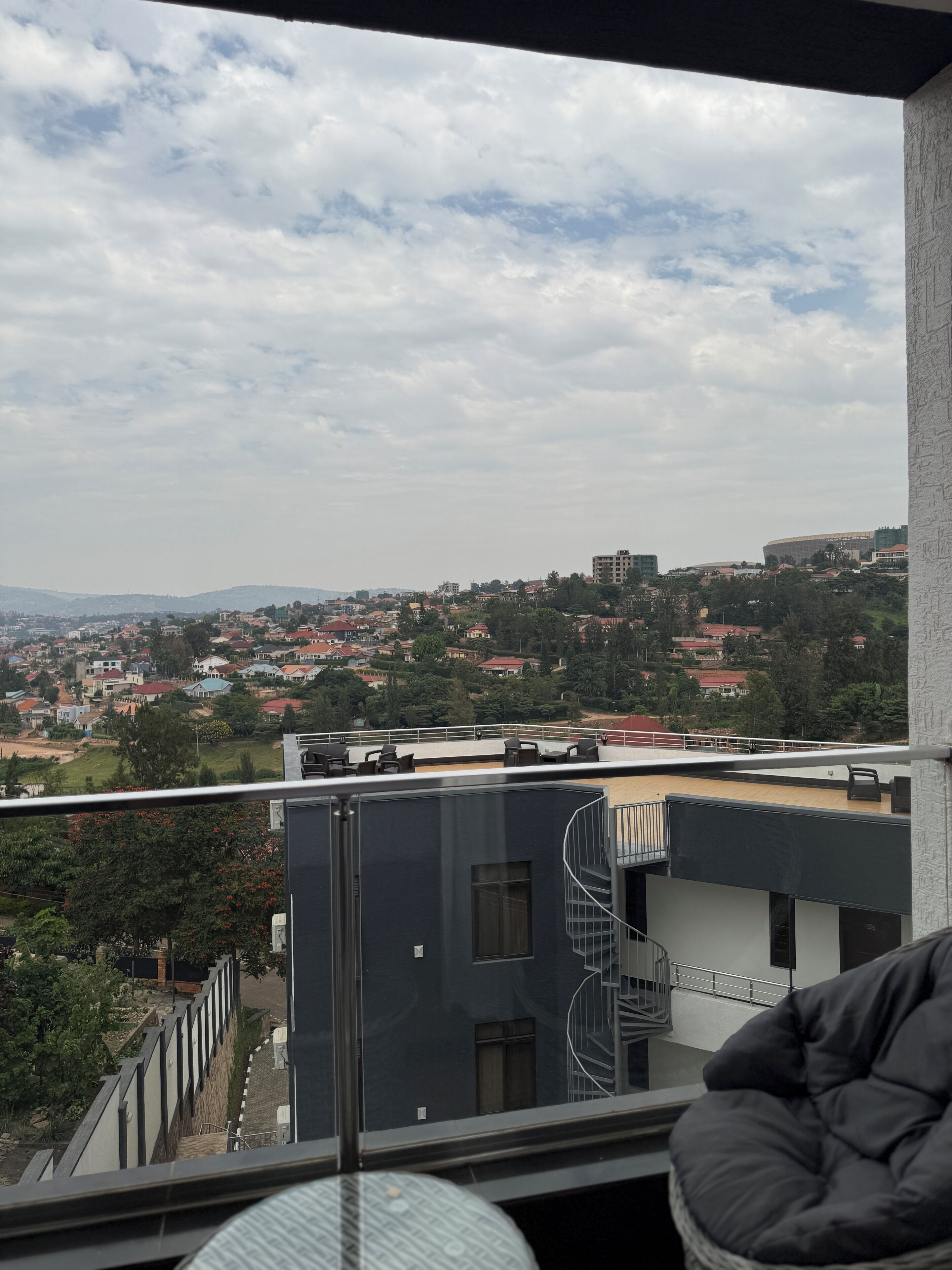 A balcony with a view of a cityscape, including buildings and a distant mountain range.