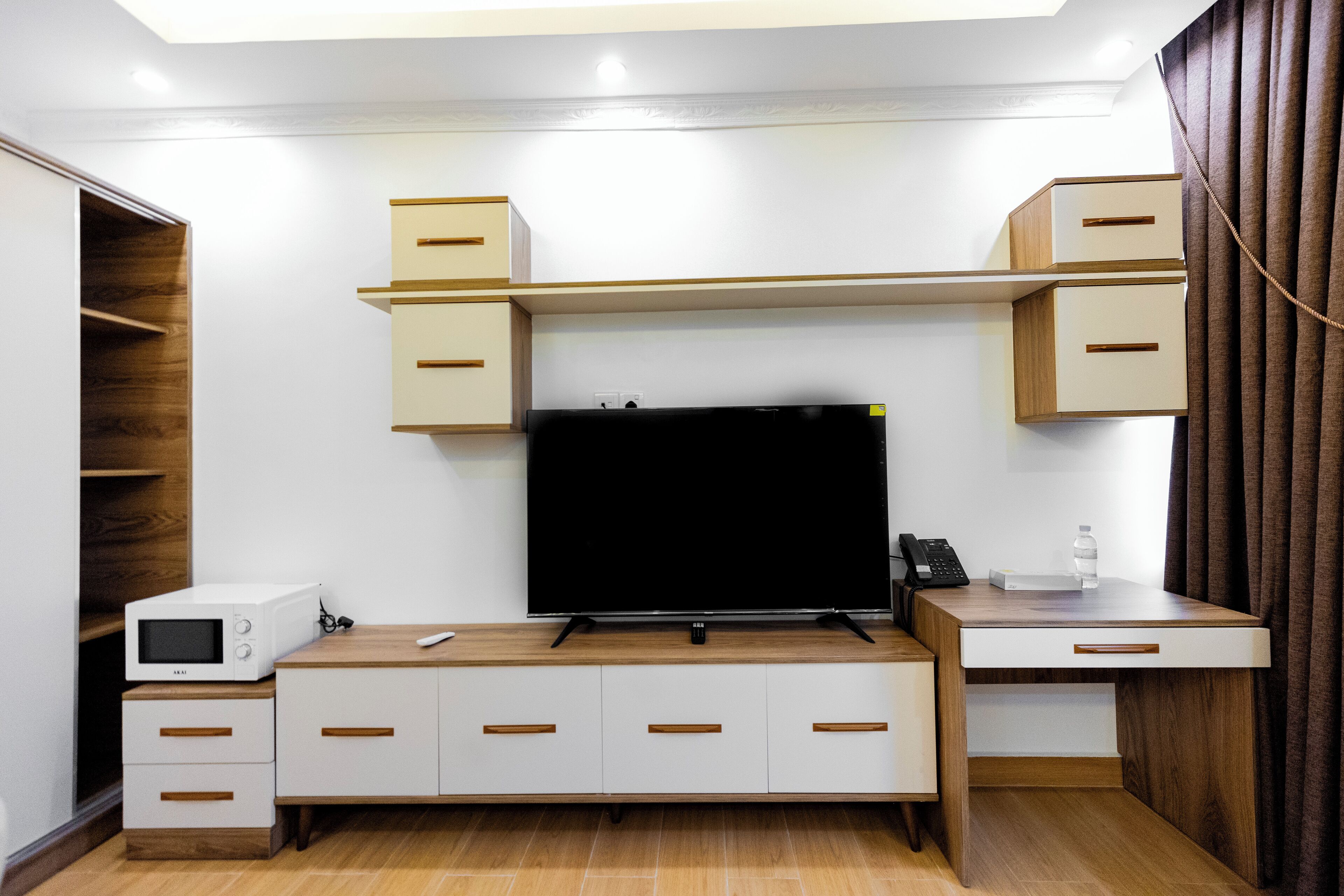 A modern room with a flat-screen TV, built-in shelving, a microwave, and a desk with drawers.