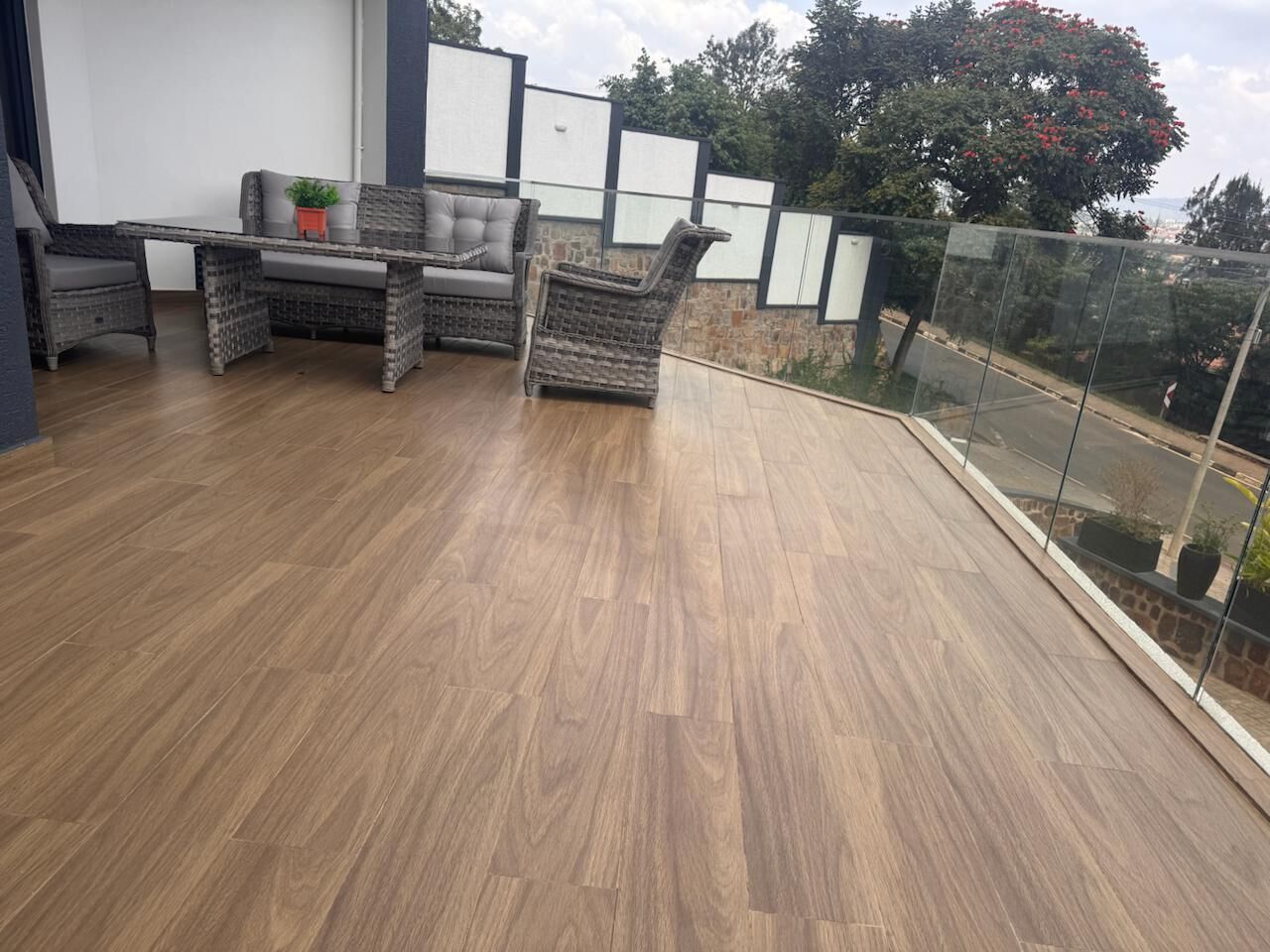 Un balcon doté d’un plancher en bois, de meubles en osier et d’une rambarde en verre.