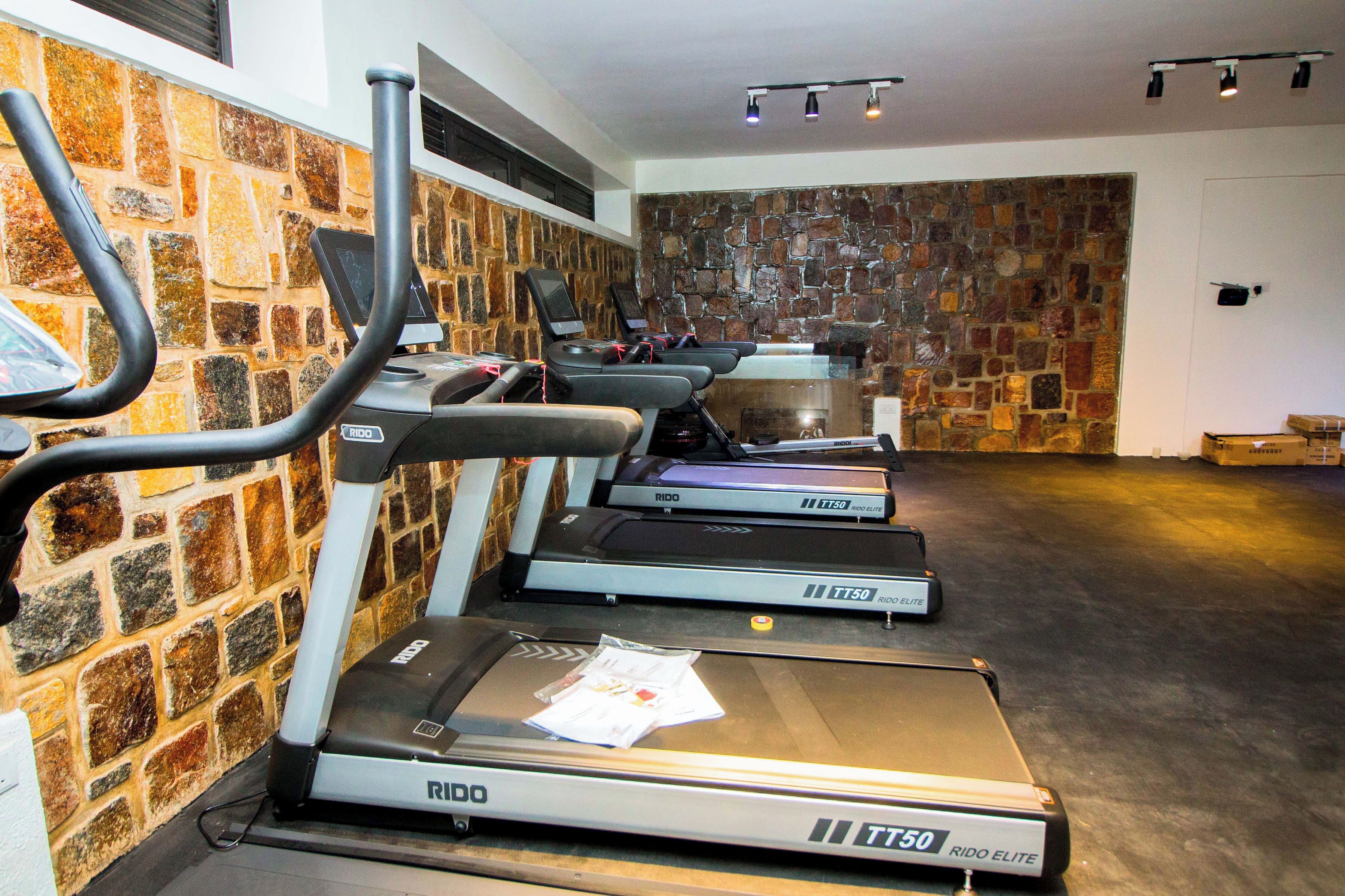 A gym with treadmills, a wall of stone tiles, and a ceiling with track lighting.