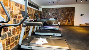 A gym with treadmills, a wall of stone tiles, and a ceiling with track lighting.