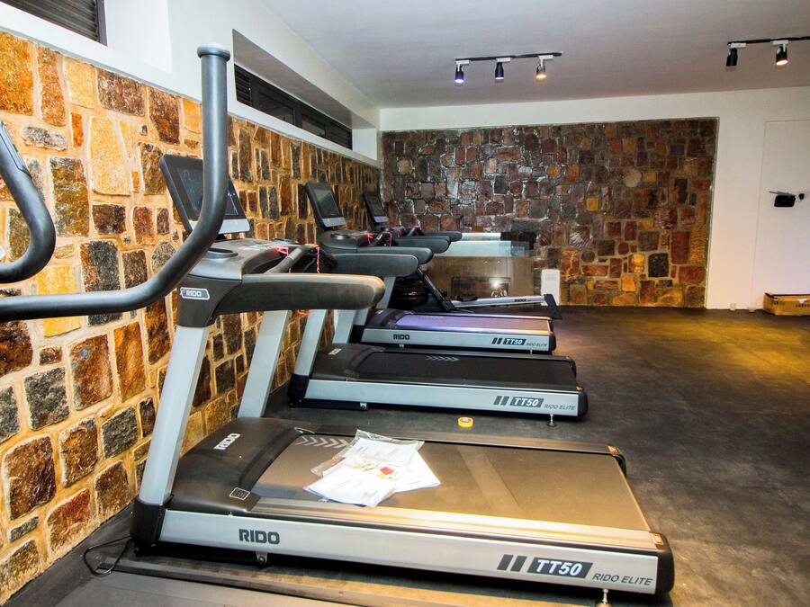 A gym with treadmills, a wall of stone tiles, and a ceiling with track lighting.