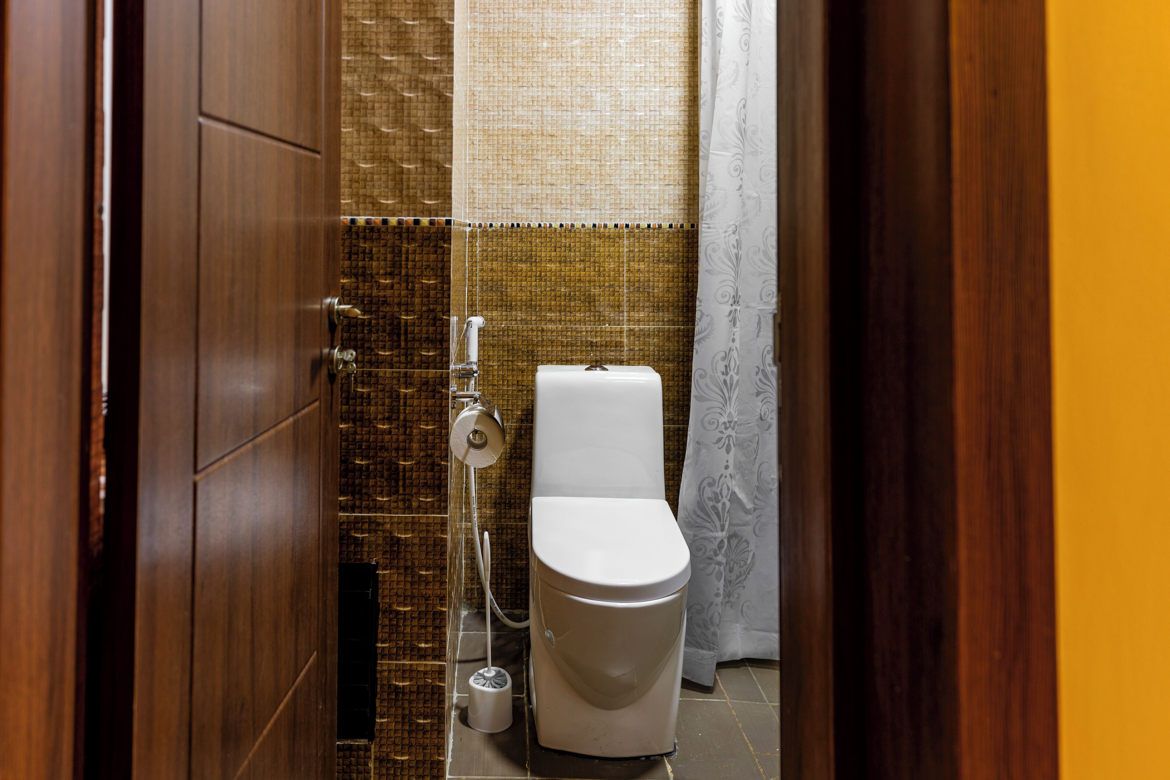 A small, compact bathroom with a toilet, a toilet paper holder, and a shower head.