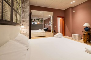 A modern hotel room with a large bed, a sliding glass door leading to a bathroom, a wooden side table with a lamp, and a brick wall accent. - Casa Polese in Bologna (Bologna)