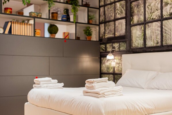 A neatly made bed with folded towels, a bookshelf with various items, and a window with a view of trees. - Casa Polese in Bologna (Bologna)