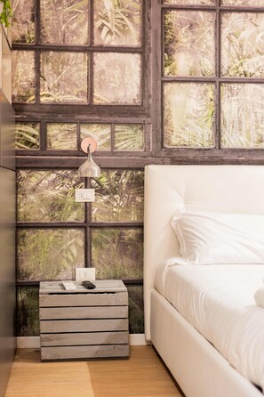 Ein Schlafzimmer mit großem Fenster, Nachttisch mit Lampe und Bett mit weißer Bettwäsche.
