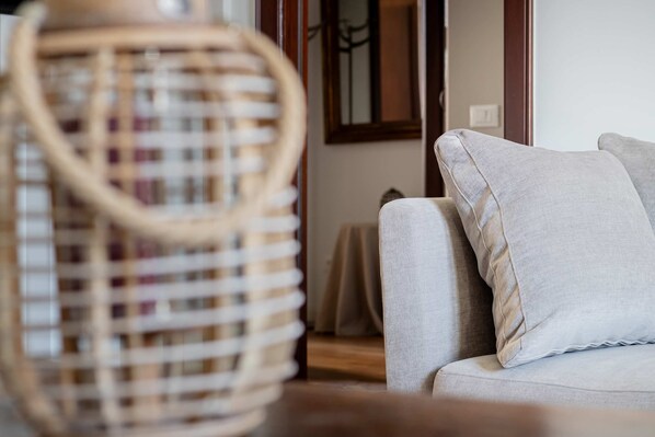 A wicker chair with a handle, a beige sofa with a pillow, and a wooden floor.
