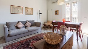 A living room with a grey sofa, a wooden coffee table, a red patterned rug, and a dining area with a table and chairs. - Casa Melzo Chic Apartment in Porta Venezia (Milan)