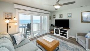 A living room with a sofa, coffee table, TV, and a balcony with a view of the ocean. - Oceanfront 2 BR Condo with Shared Pool! Channel Marker 302  (Surfside Beach)