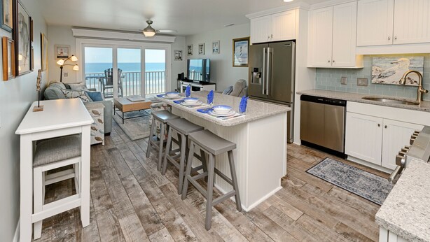 A modern kitchen with a central island, bar stools, a dishwasher, and a large refrigerator. - Oceanfront 2 BR Condo with Shared Pool! Channel Marker 302  (Surfside Beach)