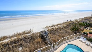 A beach view with a pool area, including a staircase leading to a deck with lounge chairs. - Oceanfront 2 BR Condo with Shared Pool! Channel Marker 302  (Surfside Beach)
