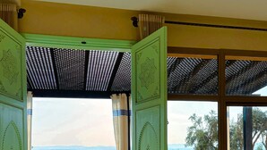 An open doorway leading to a balcony with potted plants, a view of the landscape, and a pergola structure.