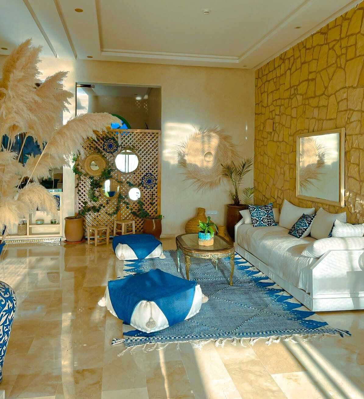 Un salon spacieux avec un canapé blanc, des coussins à motifs bleus, une table basse et des plantes décoratives.