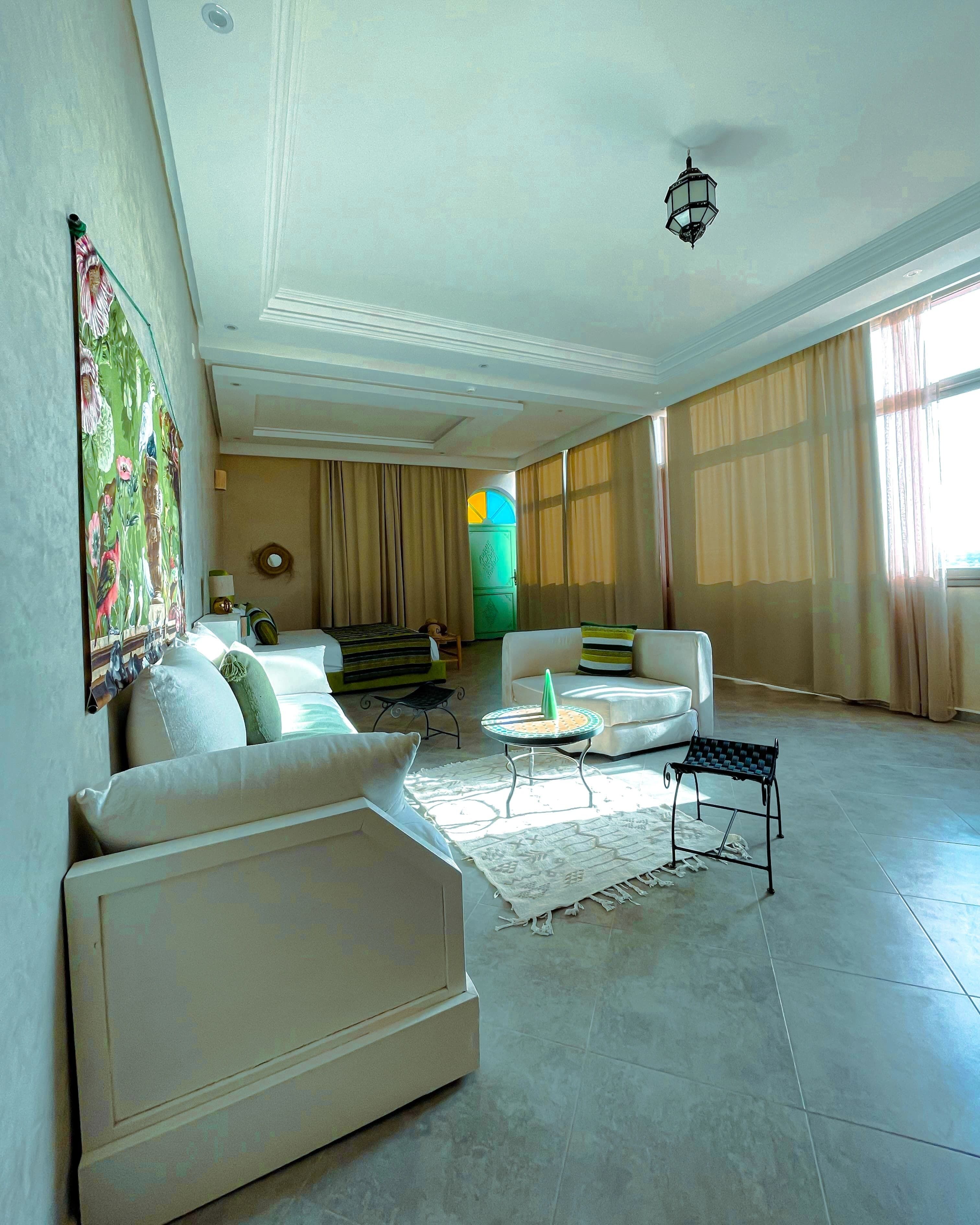 Un salon spacieux avec un grand canapé, une table basse et une petite table d’appoint. Un tableau est accroché au mur et une lampe se trouve sur la table d’appoint.