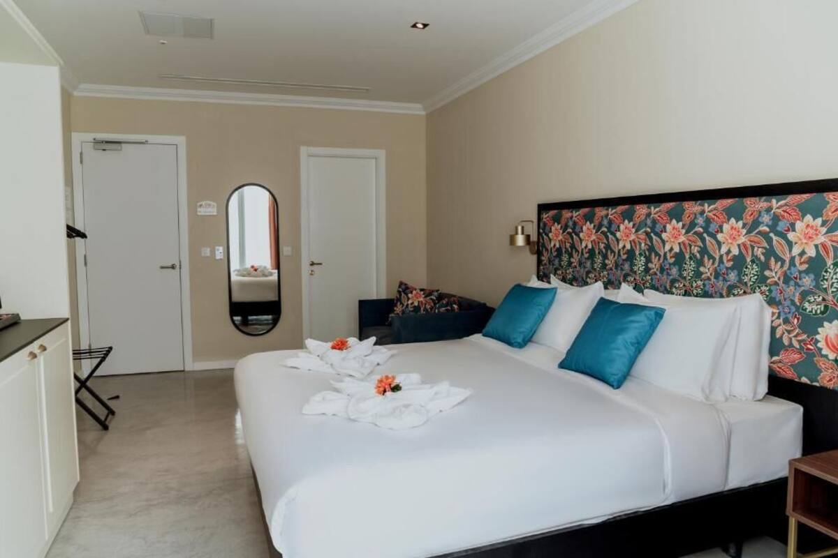 Hotellihuone, jossa on suuri sänky, työpöytä, peili ja kukkapainokuviolla koristeltu sängynpääty.