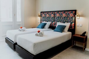 A hotel room with two beds, each with white linens and blue pillows, a floral headboard, and bedside lamps.