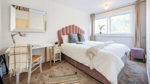 Ein Schlafzimmer mit Bett, Schreibtisch, Stuhl, Spiegel und einem Fenster mit Vorhängen.