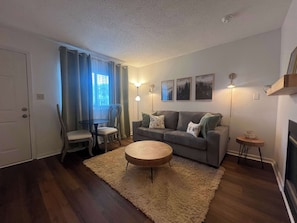 A living room with a sofa, a round coffee table, a small side table, a chair, a fireplace, and a window with curtains. - Chic Condo for 4, w/Shared Pool Near Downtown! (Gatlinburg)