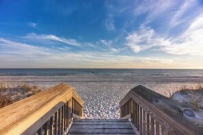 A wooden staircase leading down to a beach with a clear sky above.