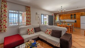 Een woonkamer met een bank, een rode poef en een eethoek met een tafel en stoelen.